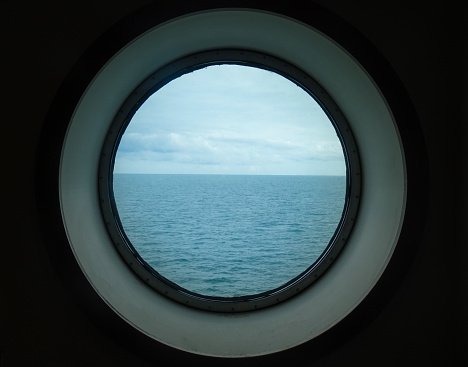 Seeing the horizon and the sea through a retro round ship window in Calais, Hauts-de-France, France