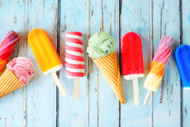 Selection of colorful summer popsicles and ice cream treats scattered on rustic blue wood stock photo