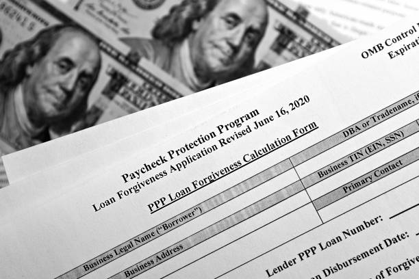 selective focus monochrome photo of paycheck protection program loan forgiveness application form revised, on a background of dollar bills stock photo