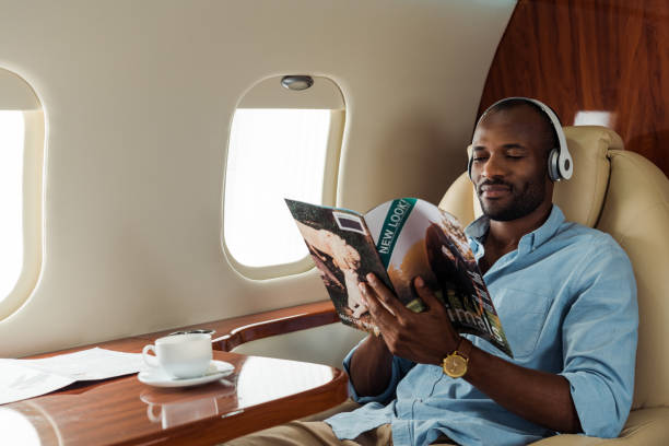 selective focus of african american man in wireless headphones reading magazine in private plane selective focus of african american man in wireless headphones reading magazine in private plane private airplane stock pictures, royalty-free photos & images