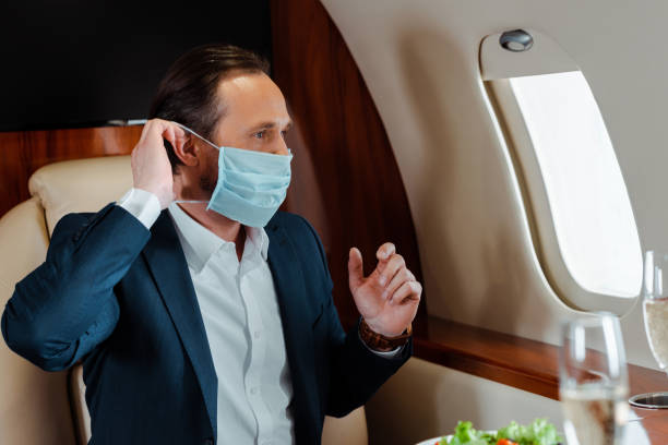 Selective focus of businessman putting on medical mask near champagne and salad on table in airplane Selective focus of businessman putting on medical mask near champagne and salad on table in airplane private plane stock pictures, royalty-free photos & images