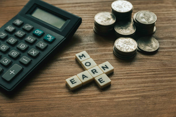 Selective focus of stack of coins,calculator and crossword alphabet of word Earn More on wooden background.  earn more stock pictures, royalty-free photos & images