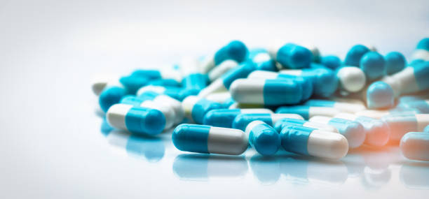 Selective focus on blue and white capsules pill spread on white background with shadow. Global healthcare concept. Antibiotics drug resistance. Antimicrobial capsule pills. Pharmaceutical industry. Selective focus on blue and white capsules pill spread on white background with shadow. Global healthcare concept. Antibiotics drug resistance. Antimicrobial capsule pills. Pharmaceutical industry. pics for amoxicillin stock pictures, royalty-free photos & images