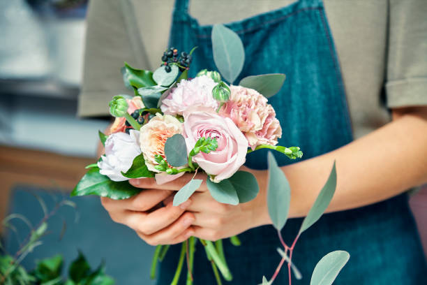 Selective focus on flower bouquet in female hands. Florist woman making bunch at shop. Flower shop, business, sale and floristry concept. Copy space for design stock photo