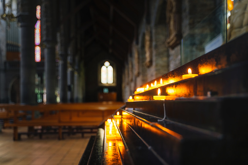 Selective focus on votive lit candle with bright soft glow and blurred background of interior of St. Marys Cathedral in Killarney, Kerry, Ireland