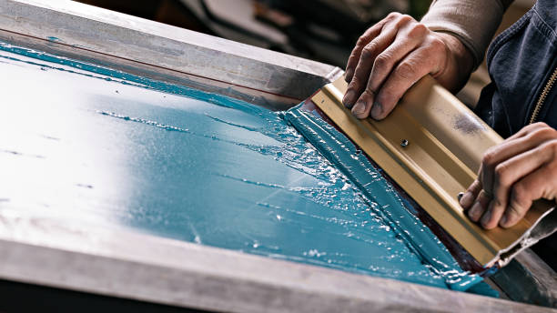 selective focus photo of male hands with squeegee. serigraphy production. printing images on t-shirts by silkscreen method in a design studio stock photo