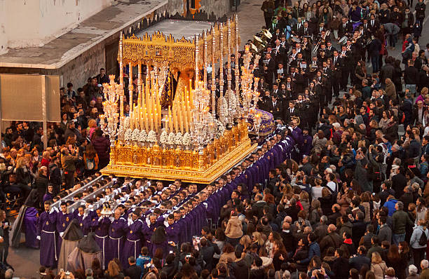 Semana Santa in Malaga: procession of Rescate brotherhood Malaga, Spain - March 22, 2016: eight rows of men dressed in purple robes, carry a heavy float with a statue of Virgin Mary, richly decoarted with golden ornaments and burning candles, in the Easter procession of the Rescate brotherhood on holy Tuesday. The procession is watched by many spectators .  holy week stock pictures, royalty-free photos & images