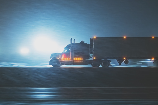 Semi truck on a multi lane highway during heavy snowfall at night. Photographed at high iso with slight motion blur in some points of the frame.