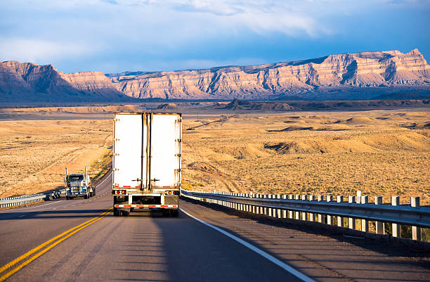 Semi trucks with trailers carrying cargo on the highway Semi trucks with dry van and flat bed trailers carrying cargo on the highway with security fencing in Utah in the sun-lit mountain ranges and yellow lowland hills semi truck back stock pictures, royalty-free photos & images
