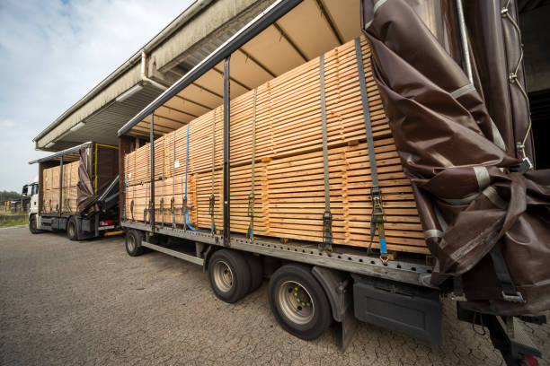木および木の建築材料のための倉庫の積み重ねられた木製の板が付いたセミトラックおよびトレーラー。青い空、屋外。