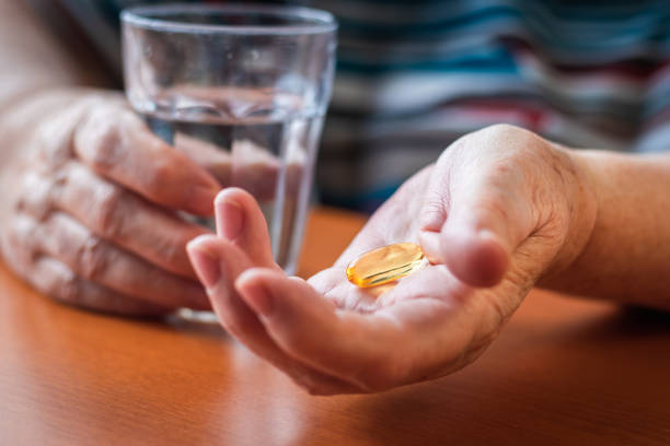 Senior adult woman taking fish oil capsule. Omega-3 pill and glass of water in senior female hands. Medical and health care concept with people fish oil stock pictures, royalty-free photos & images
