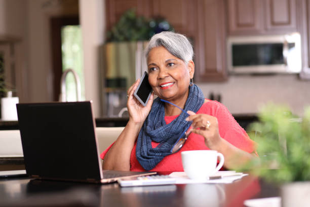 Senior adult woman using phone and laptop at home. stock photo