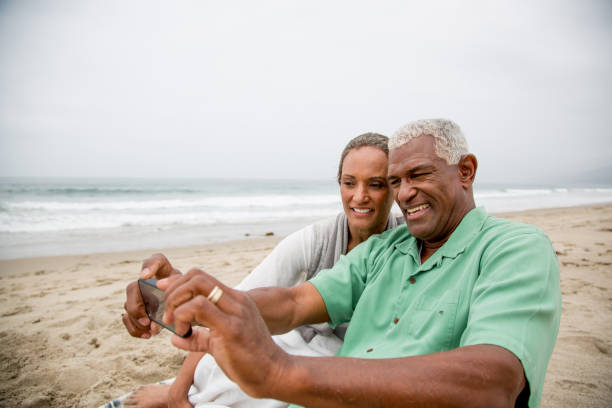 Senior African American couple having fun with smartphone on beach Senior African American couple having fun photographing self portrait with smartphone on sandy beach. old black couple in love stock pictures, royalty-free photos & images