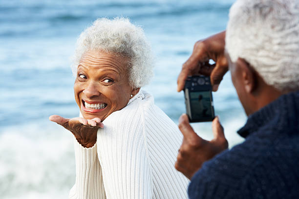 Senior African American couple taking photos at the beach Senior Couple Taking A Photo With Camera On Beach old black couple in love stock pictures, royalty-free photos & images