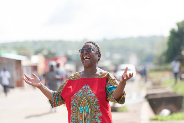 Senior African woman laughing hands raised on rural street stock photo
