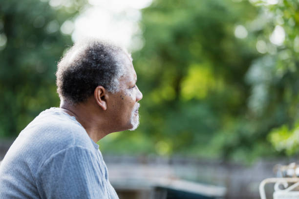Senior African-American man outdoors, thinking A senior man sitting outdoors in his back yard with a sad expression on his face, looking out into the distance. He is an African-American man in his 60s. sad old black man stock pictures, royalty-free photos & images