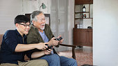 彼の居心地の良い家で彼の息子とビデオゲーム機を楽しんで定年のシニアアジアの男性