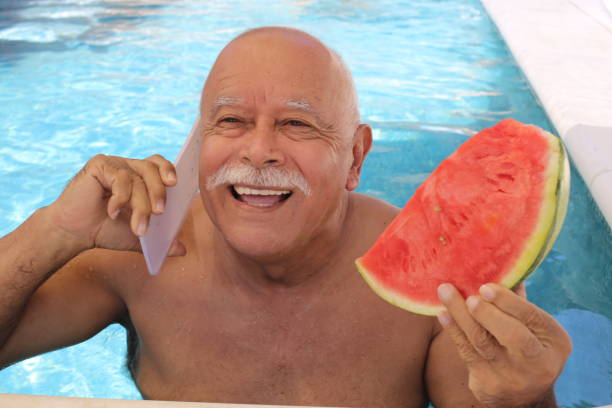 senior bald guy with a mustache using phone in swimming pool - bald beach imagens e fotografias de stock