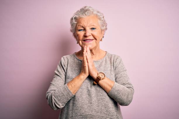 Senior beautiful woman wearing casual t-shirt standing over isolated pink background praying with hands together asking for forgiveness smiling confident.  prayer request stock pictures, royalty-free photos & images