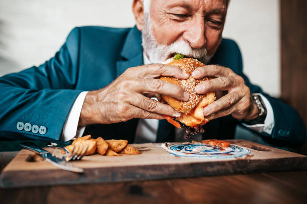 homme d’affaires aîné à la table de restaurant - eating burger photos et images de collection