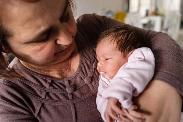 Senior caucasian woman grandmother hold newborn infant girl vomiting milk - baby overfeeding puke milk in hands of her granny at home - new life nursing and growing up concept  baby's reflux stock pictures, royalty-free photos & images