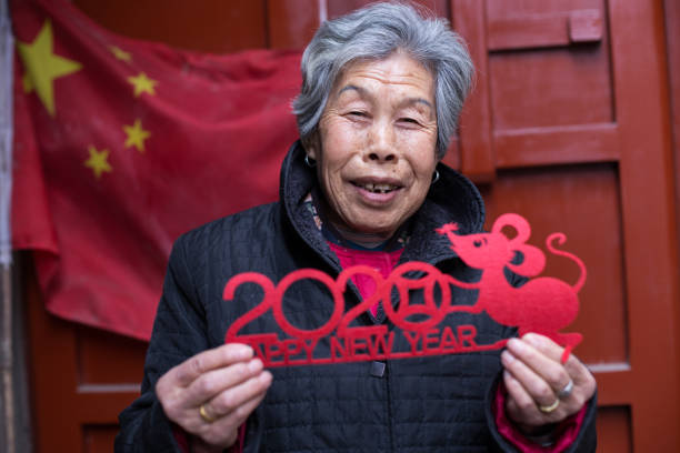 A senior Chinese woman smiles to the camera and prepares Chinese traditional paper cuts for decoration for Chinese New Year in Beijing, China. stock photo