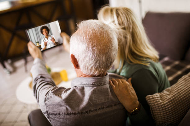 Senior couple at home holding digital tablet during video call with family doctor stock photo
