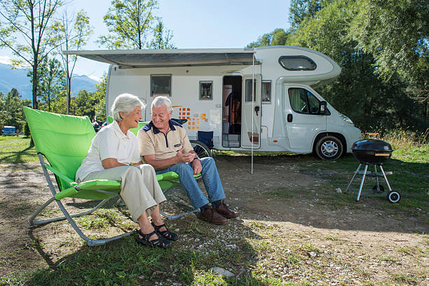 Senior couple having fun camping with camper van Senior couple sitting in front of camper van and having fun rv stock pictures, royalty-free photos & images