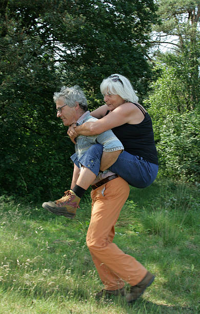 senior couple having fun outdoors - piggyback funny stockfoto's en -beelden