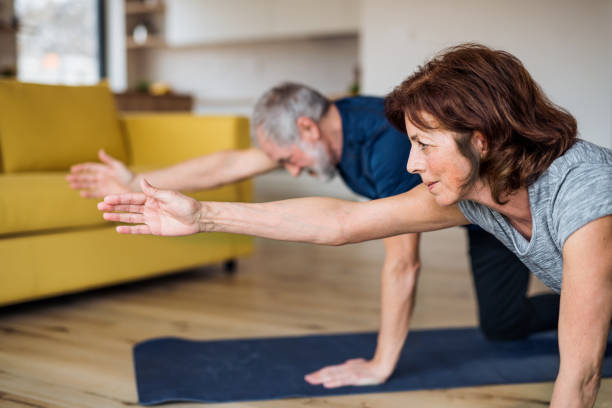 A senior couple indoors at home, doing exercise on the floor. A happy senior couple indoors at home, doing exercise on the floor. relaxation exercise stock pictures, royalty-free photos & images