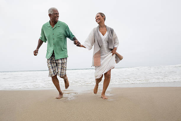 senior couple on the beach - hardlopen vorouw stockfoto's en -beelden