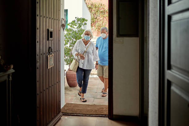 Senior Couple Returning Home Wearing Protective Face Masks View from inside front door of casual Caucasian couple in 50s and 60s wearing protective face masks and returning home from errands in time of COVID-19. approaching photos stock pictures, royalty-free photos & images