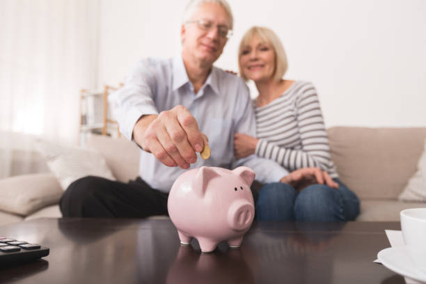 coppia senior risparmia denaro in salvadanaio a casa - fondo pensionistico personale foto e immagini stock