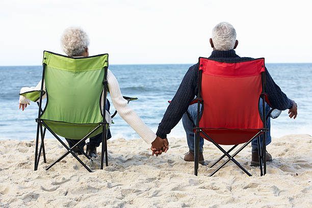 Senior Couple Sitting On Beach In Deck chairs Senior Couple Sitting On Beach In Deck chairs Holding Hands old black couple in love stock pictures, royalty-free photos & images