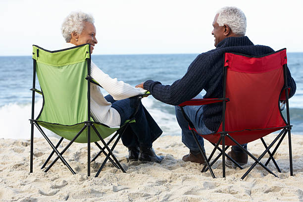Senior Couple Sitting On Beach In Deckchairs Senior Couple Sitting On Beach In Deckchairs Holding Hands Looking At Each Other old black couple in love stock pictures, royalty-free photos & images