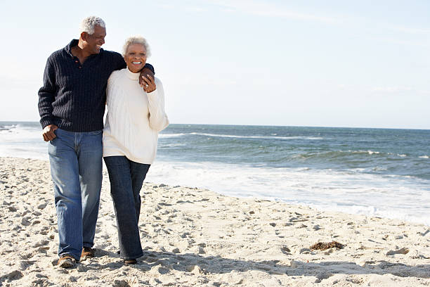 Senior Couple Walking Along Beach Together Senior Couple Walking Along Beach Together In Daytime Talking old black couple in love stock pictures, royalty-free photos & images