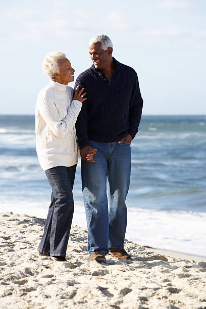 Senior Couple Walking Along Beach Together Senior Couple Walking Along Beach Together Smiling To Each Other old black couple in love stock pictures, royalty-free photos & images