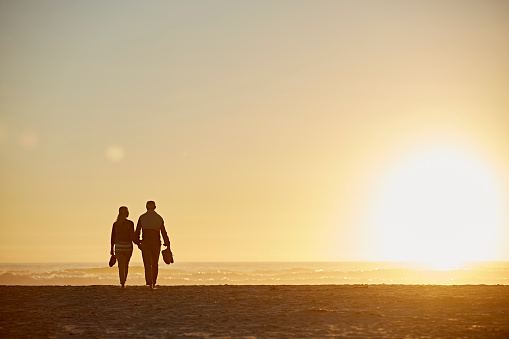 Full length rear view of senior couple walking on beach during sunset