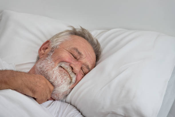 Senior elderly man sleeping happily with white blanket in bedroom stock photo