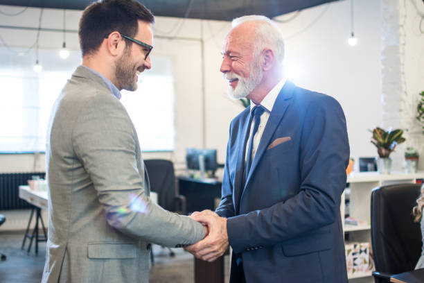 Senior executive shaking hands with young employee at office stock photo