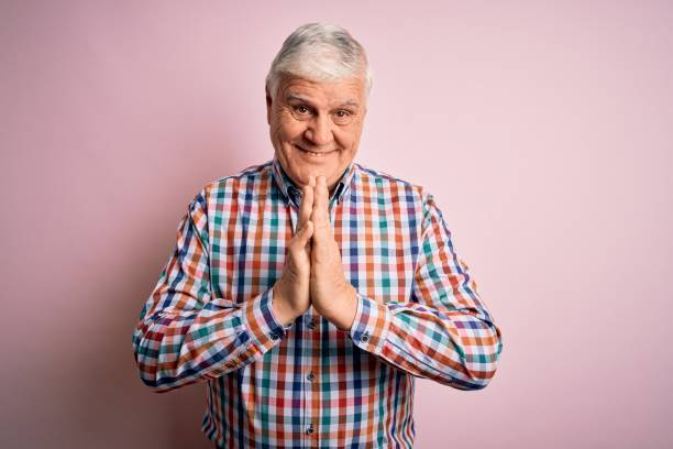 Senior handsome hoary man wearing casual colorful shirt over isolated pink background praying with hands together asking for forgiveness smiling confident.  prayer request stock pictures, royalty-free photos & images