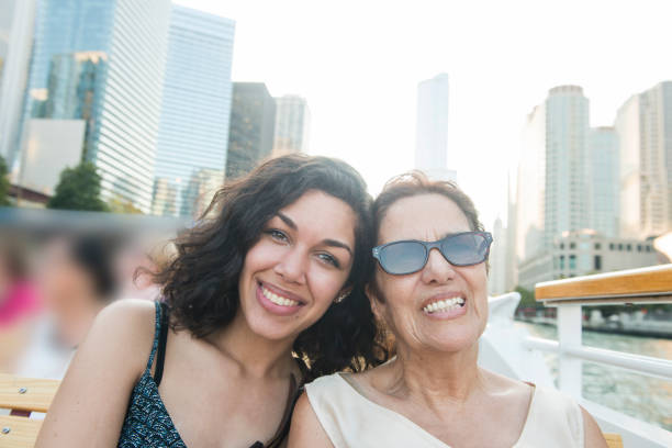 Senior Hispanic Woman and Millennial Granddaughter on Chicago Boat Tour This is a horizontal, color photograph of a two beautiful Puerto Rican women from different generations are enjoying a boat tour in Chicago, Illinois, a major USA city in the Midwest. The senior grandmother and Millennial granddaughter pose together, smiling as they look at the camera. Buildings along the Chicago River fill the background. hot puerto rican woman stock pictures, royalty-free photos & images