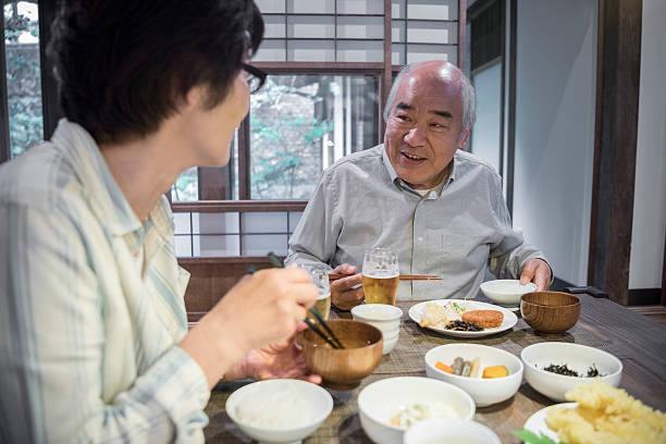 Senior Japanese man taling to woman over dinner Japanese couple eating dinner together at home, bowls of food on table, senior man listening to woman senior couple photos stock pictures, royalty-free photos & images