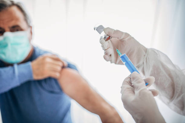 Senior male is about to receive Covid-19 coronavirus vaccine Two people, medical doctor in protective suit giving a senior male Covid-19 coronavirus vaccine. preventative medicine stock pictures, royalty-free photos & images
