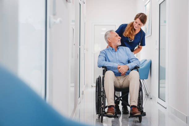 Senior male patient sitting in wheelchair in hospital corridor with female nurse doctor Senior male patient sitting in wheelchair in hospital corridor with female nurse doctor female nurse stock pictures, royalty-free photos & images