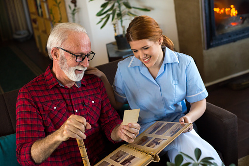 Senior man bonding with nurse in the nursing home. Showing photo album with childhood photographs.