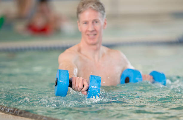 Senior Man doing Water Aerobics A senior adult working out with water dumbbells in an indoor pool - practicing water aerobics and aquatics aquatic organism stock pictures, royalty-free photos & images