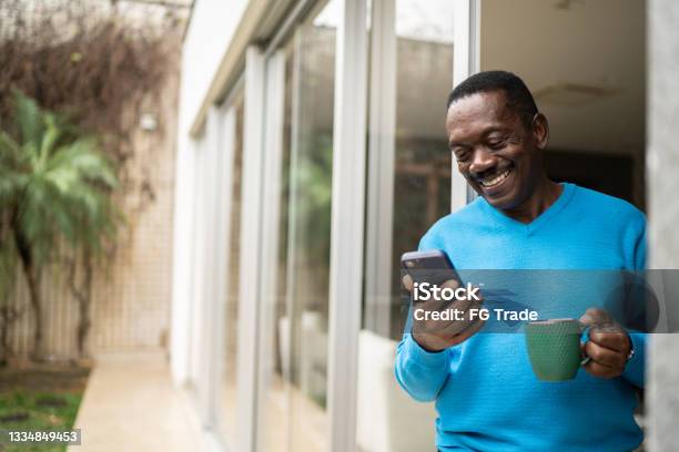 Senior man holding coffee/tea mug and using smartphone at home