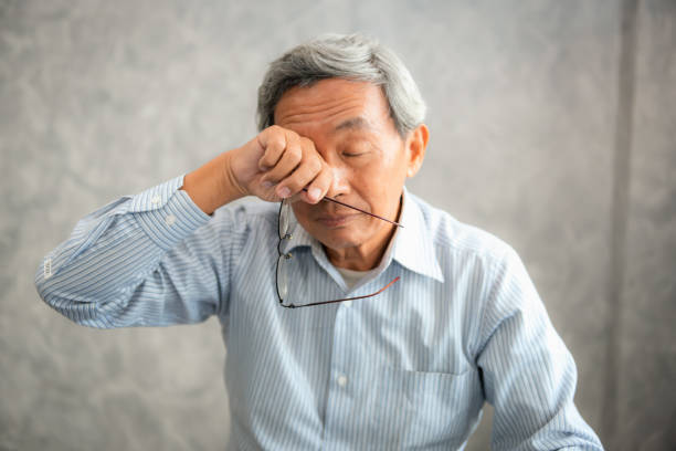 Senior man is holding eyeglasses and  rubbing his tired eyes while reading e-book in tablet stock photo