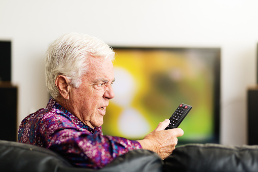 senior-man-looking-at-tv-remote-control-confused-and-irritated-picture-id1182404287